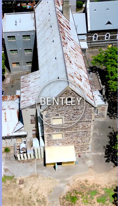 Aerial video frame of a heritage building site with the Bentley Consulting circular mark overlaid
